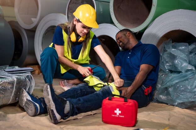 Female Safety Officer Using First Aid Kit to Help Injured Worker in Factory Emergency Situation